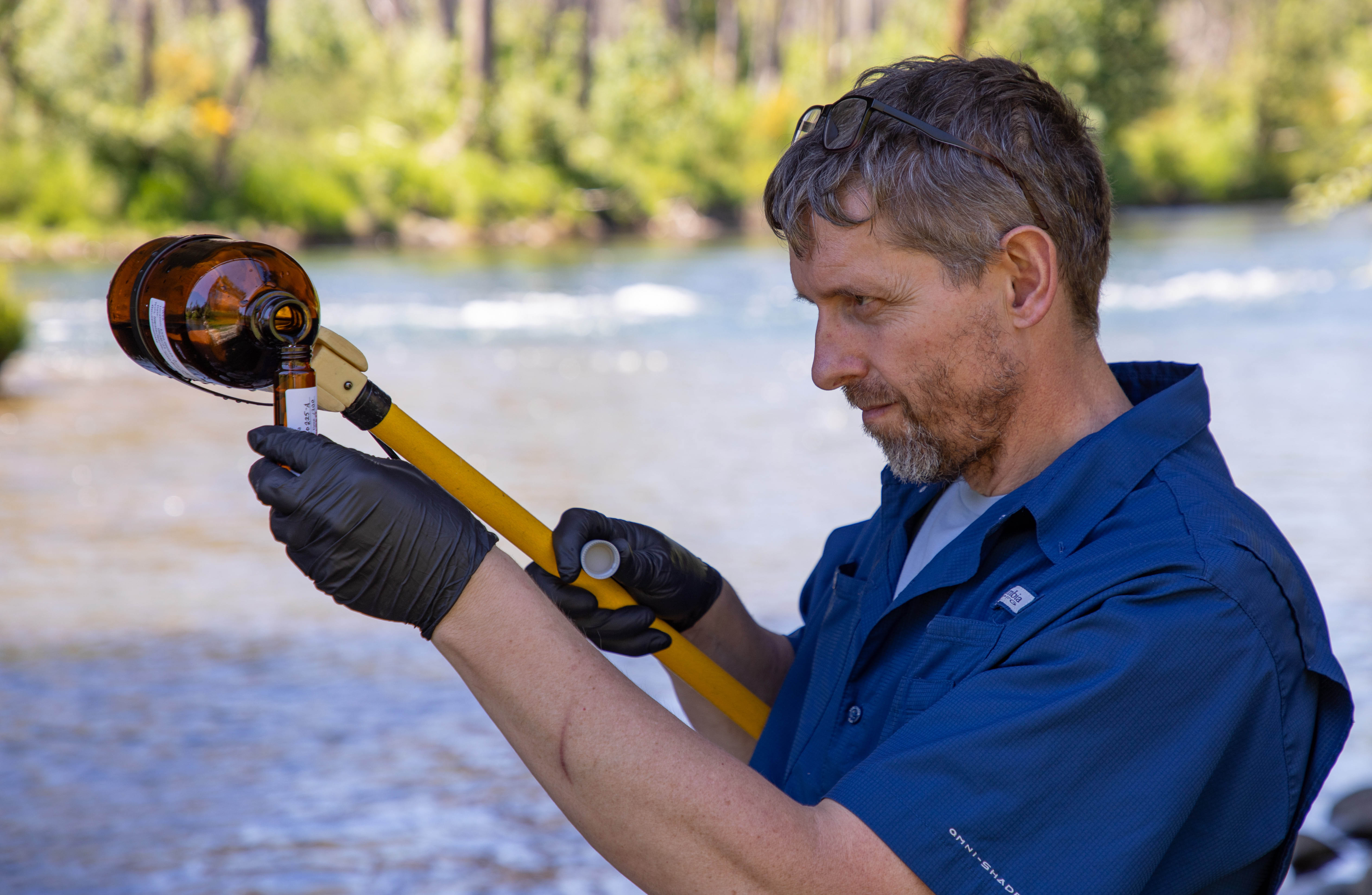 A water quality specialist pours a sample of river water into a sample bottle at Blue River and McKenzie River confluence.